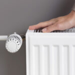 Woman warming hand near heating radiator at home, resource management during colder seasons