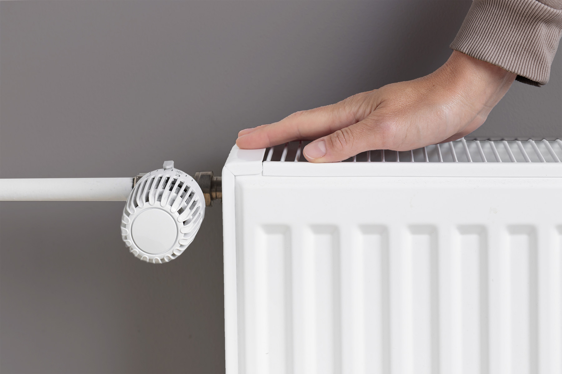 Woman warming hand near heating radiator at home, resource management during colder seasons